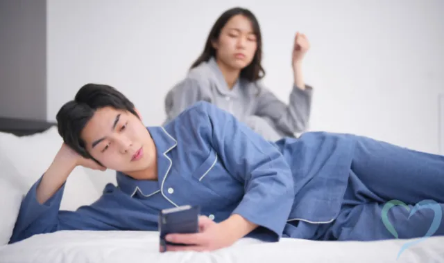 ベッドでスマホを見る男性と何かを疑う女性