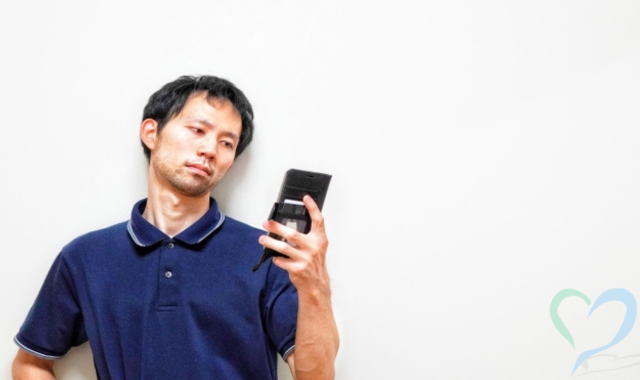 不満な表情を浮かべスマホを見る男性